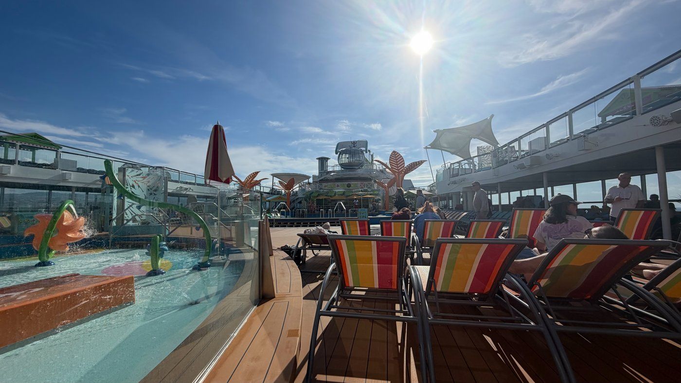 The pool deck aboard Odyssey of the Seas on embarkation day — striped loungers and the splash park in bright sun