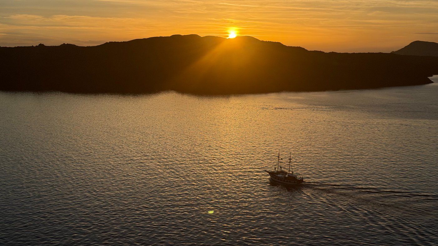 Sunset over the Santorini caldera, a small boat crossing the golden water